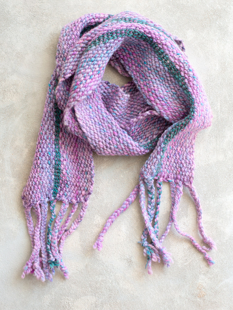 A scarf made from purple and pink yarn with a contrasting stripe of blue and gray yarn running vertically through the weave