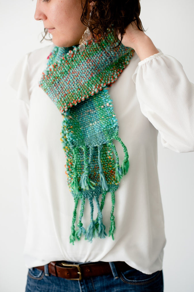 Hand woven scarf made from green and blue yarns with orange, pink, and yellow accents